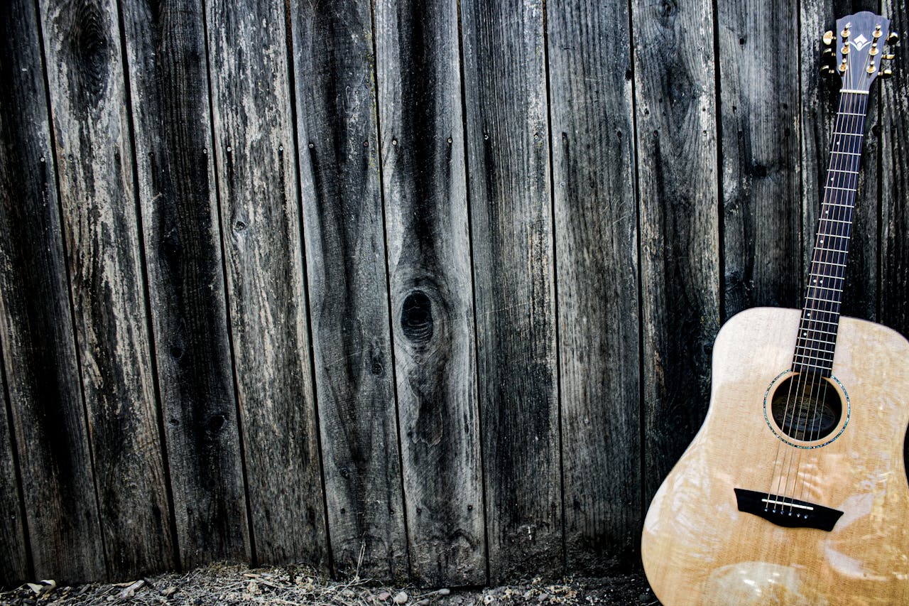 An acoustic guitar resting against a textured wooden wall, evoking a rustic musical charm.