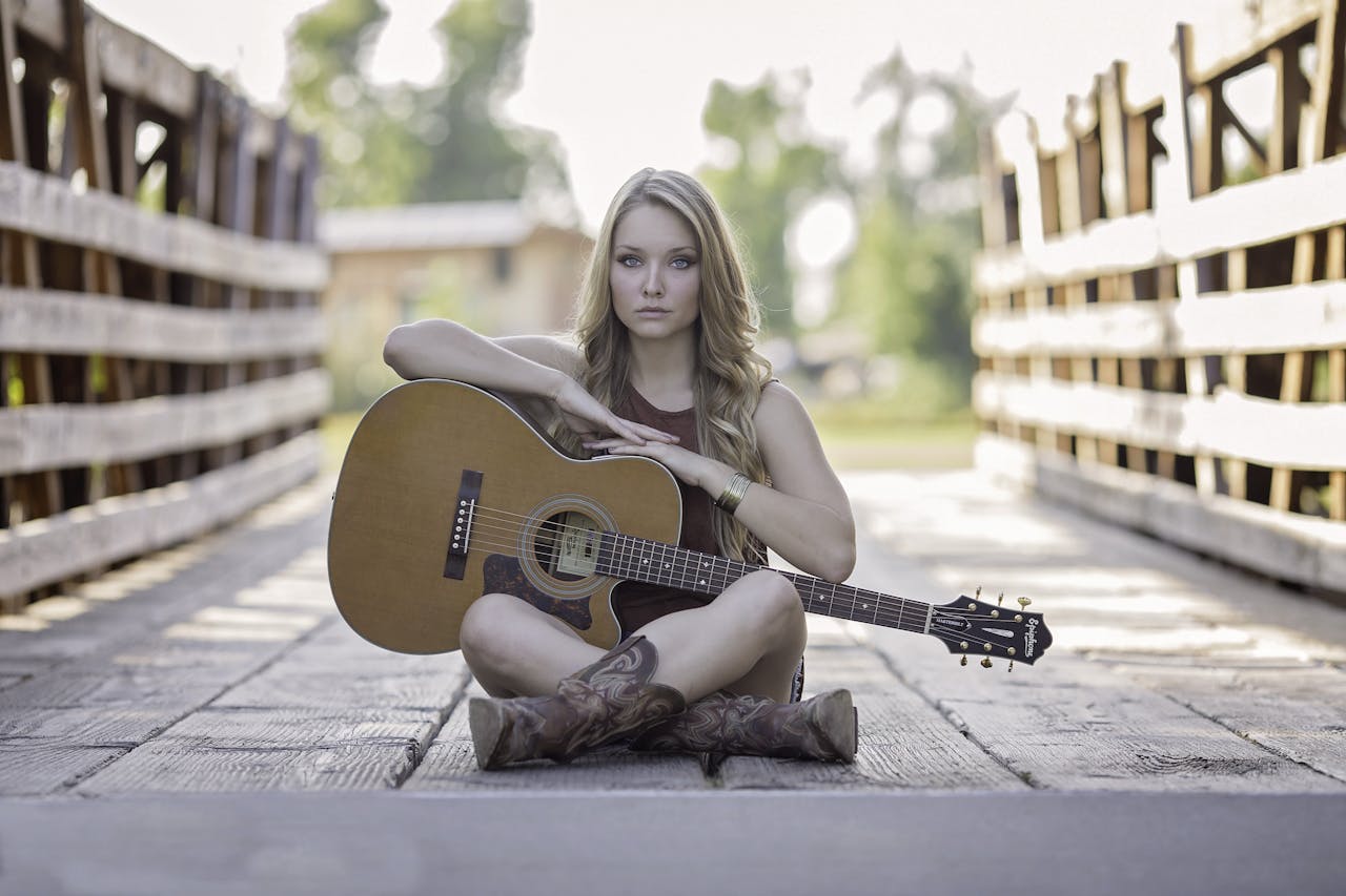 Artistic portrait of a young woman sitting with a guitar on a rustic wooden bridge.